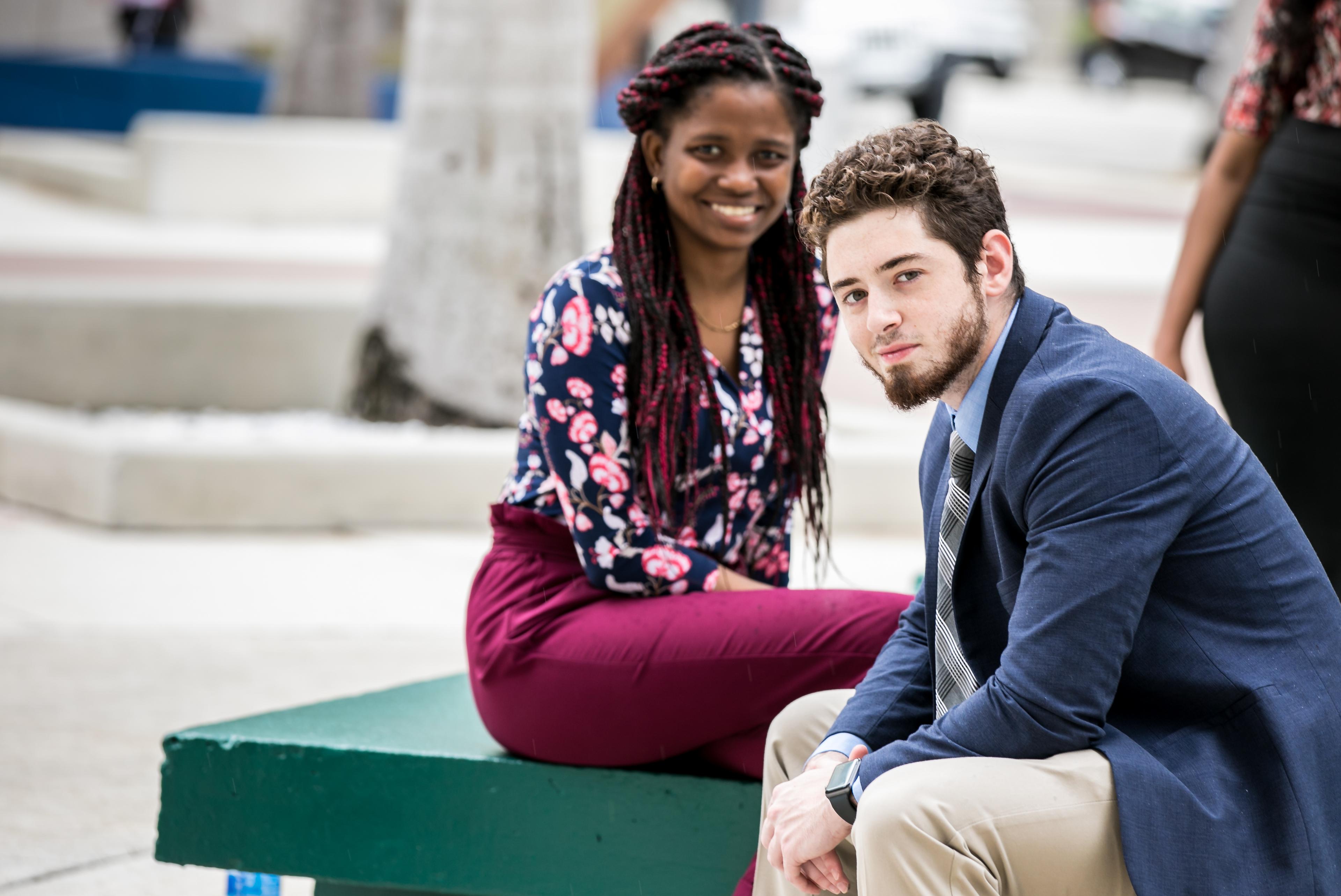 Two young adults smiling and sitting outside